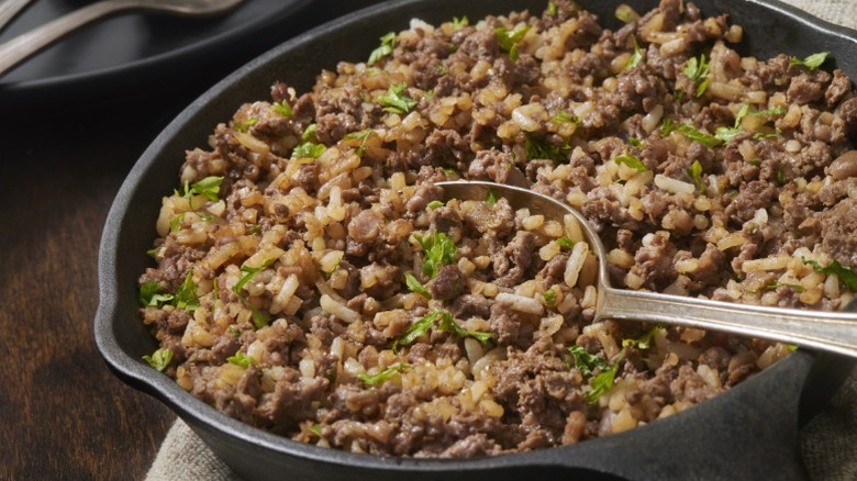 Ground beef being cooked with rice in skillet with metal spoon in it
