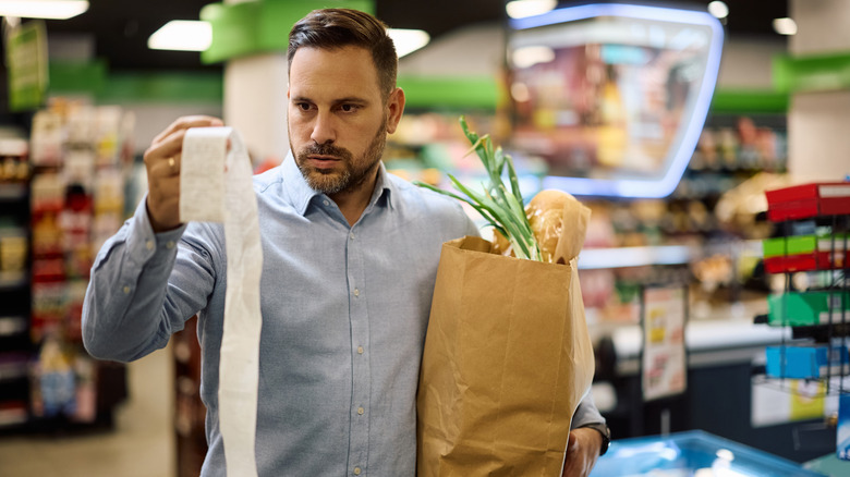 Man in grocery store looking unhappily at his receipt after purchasing groceries