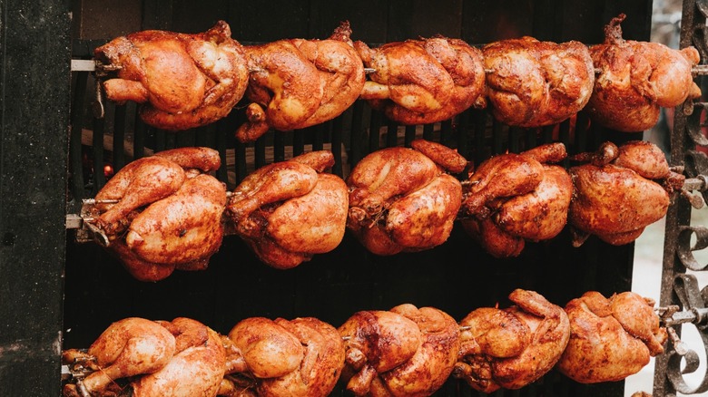 Over a dozen rotisserie chickens being prepared.