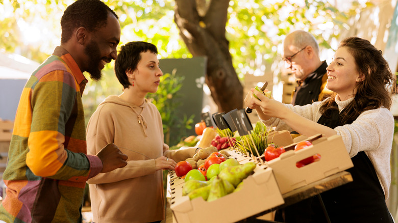 Seller cutting a fruit sample for customers at a farmers market.