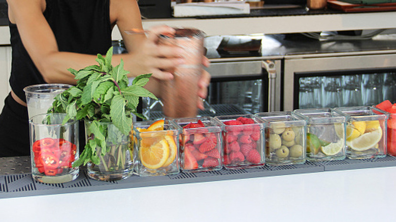 A bartender shaking a cocktail behind a bar covered with different fruit trays.