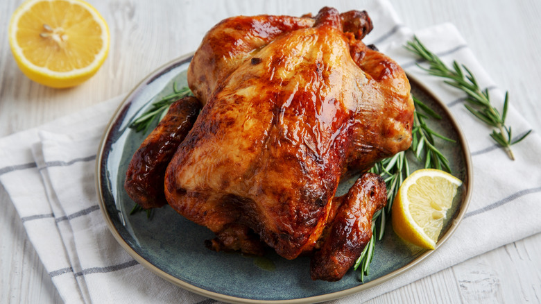 Whole roast chicken with browned crispy skin on a round light blue plate with a rosemary spring and lemon wedge