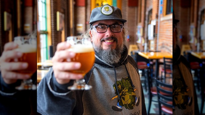 Man holding up a beer to the camera and smiling inside Bell's Brewery