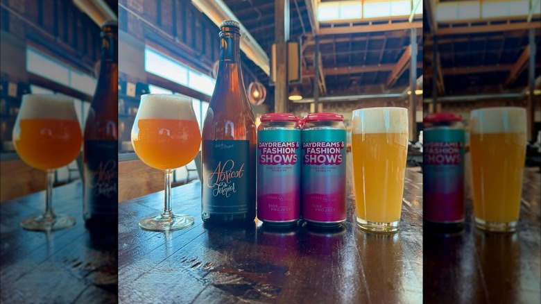 Two glasses, a bottle, and two cans of beer on a wooden table at Side Project Brewery