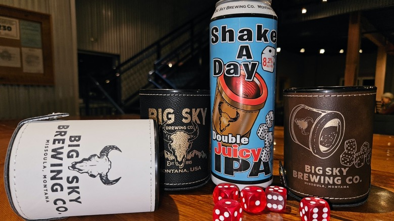 A can of beer, three cozies, and red dice on a tabletop