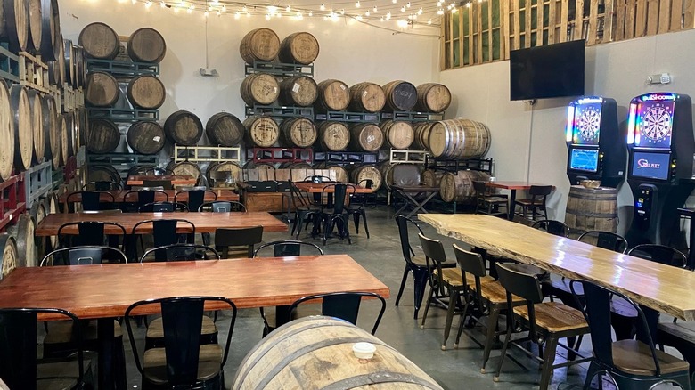 Empty interior at White Elm brewery with two darts machines, low wooden tables, and several wooden barrels lining the walls