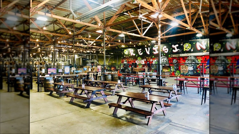 Large empty interior at Revision Brewing company, with concrete floors, picnic tables, high wooden beams, arcade games, and wall murals