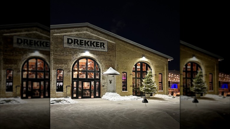 Exterior of Drekker Brewing in brick building at night with christmas tree at entrance and snow on ground