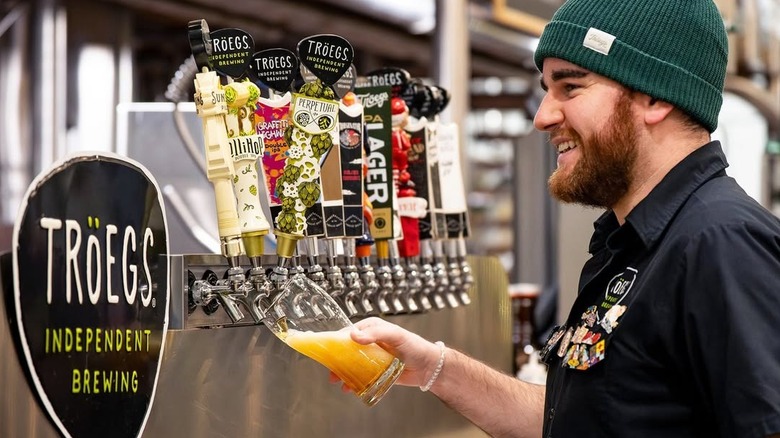 Smiling bartender with beard pouring out beer from tap at Troegs Brewery