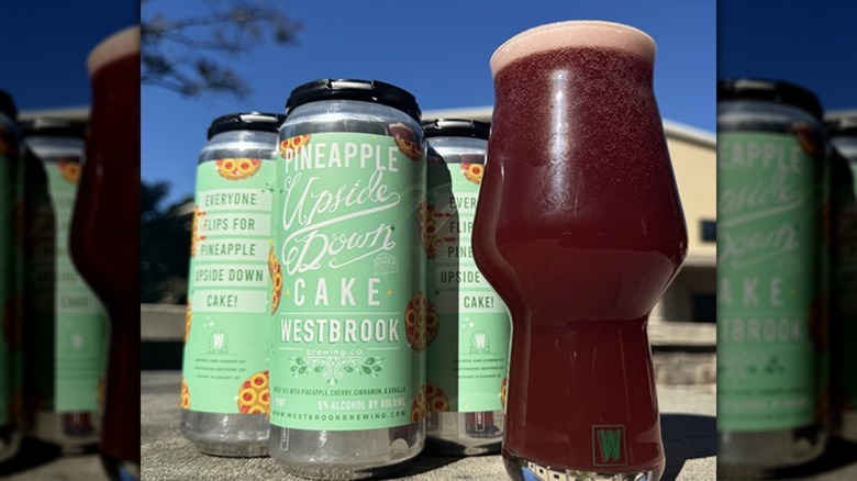 Three cans of tallboy beers next to poured glass outside on a tapletop