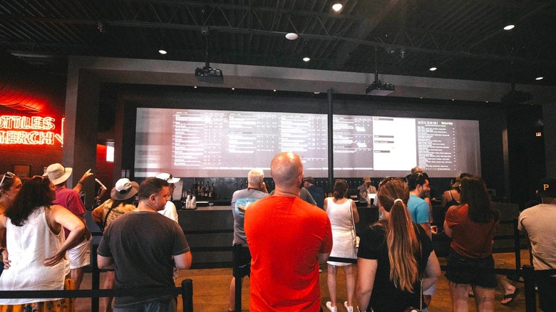 Crowded interior of The Veil Brewery with customers lining up to order from long beer menu behind counter