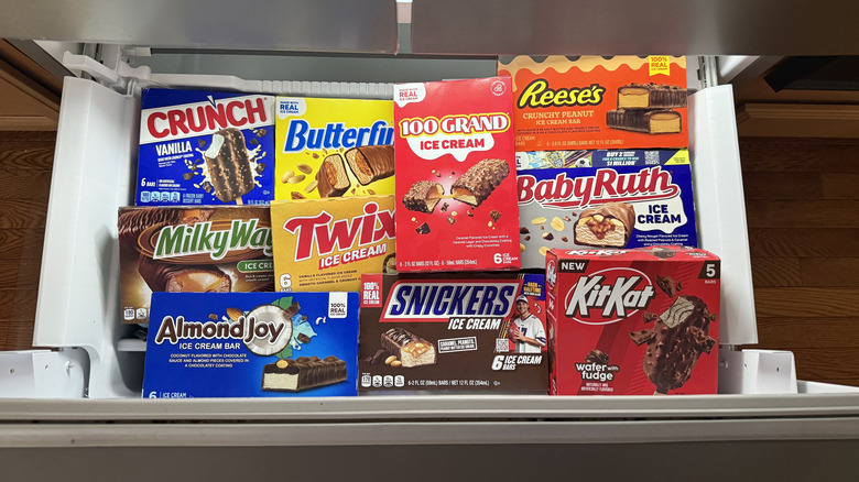 Assorted frozen candy bar ice creams in drawer-style freezer.