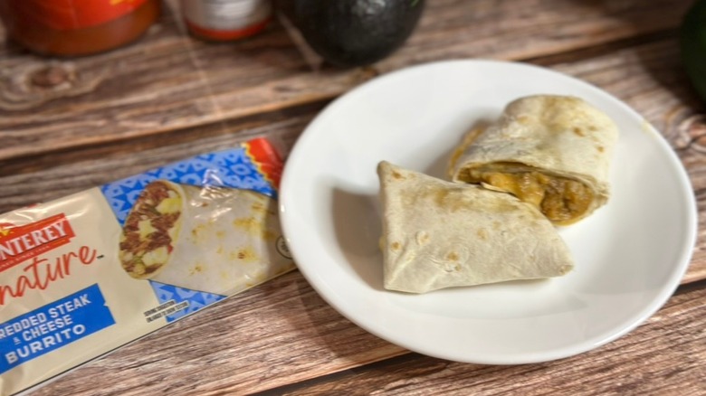 El Monterey beef burrito sitting on a small plate next to an empty wrapper on a table.