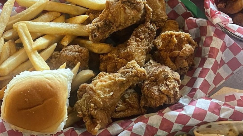 Pile of fried chicken wings next to fries and a roll in a basket with checkered paper
