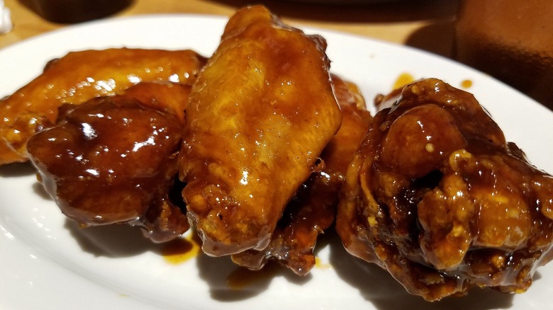 Three incredibly saucy chicken wings on a white plate