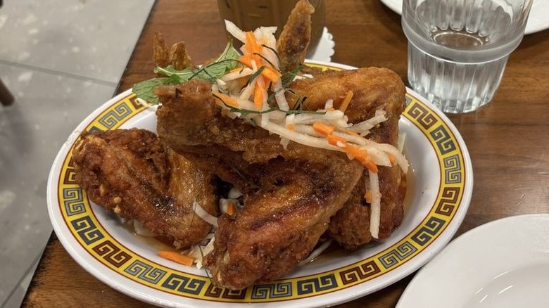 Plate of fried chicken wings topped with pickled radish, carrots, and peanuts