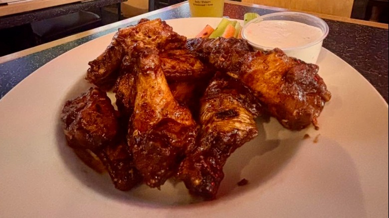 Pile of chicken wings next to celery and carrots with a side of ranch dressing on a white plate