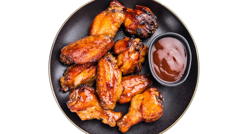 Black bowl of chicken wings next to some sauce