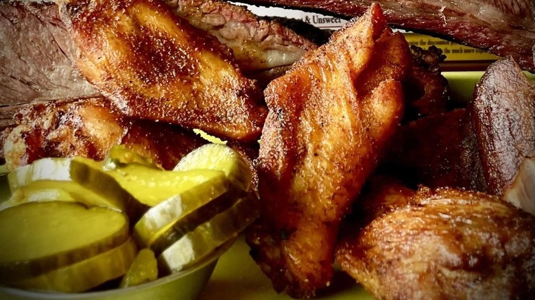 Fried chicken wings next to a small bowl of pickles and some brisket