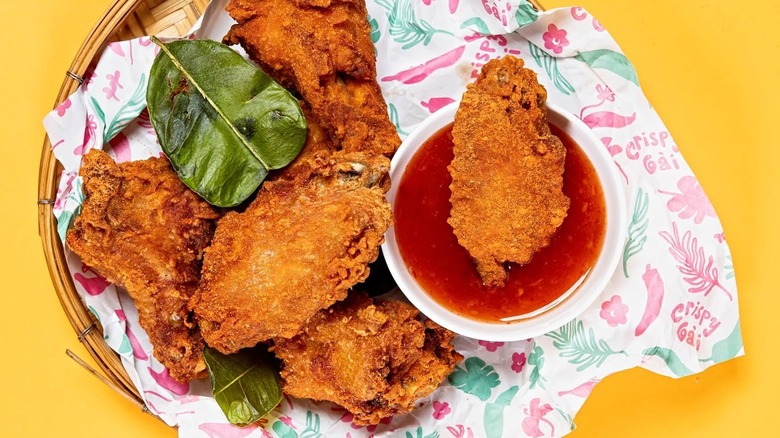 Wooden plate with fried chicken wings and garnish with one wing being dunked in red sauce