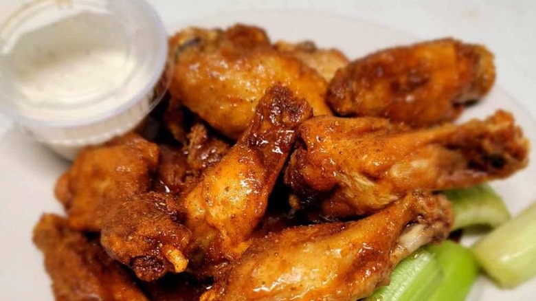 Pile of chicken wings next to ranch and celery sticks on a white plate