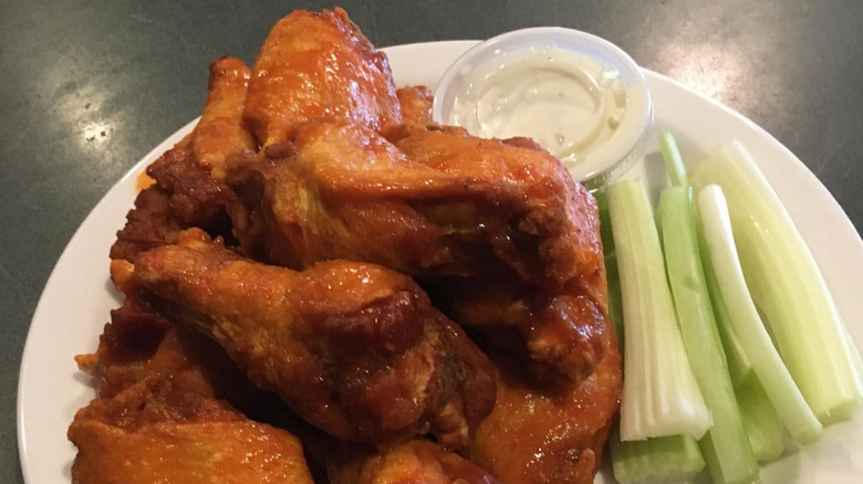 pile of buffalo wings on a white plate next to ranch and celery
