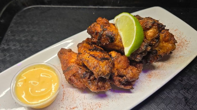 White plate of seasoned chicken wings next to sauce and topped with lime wedge