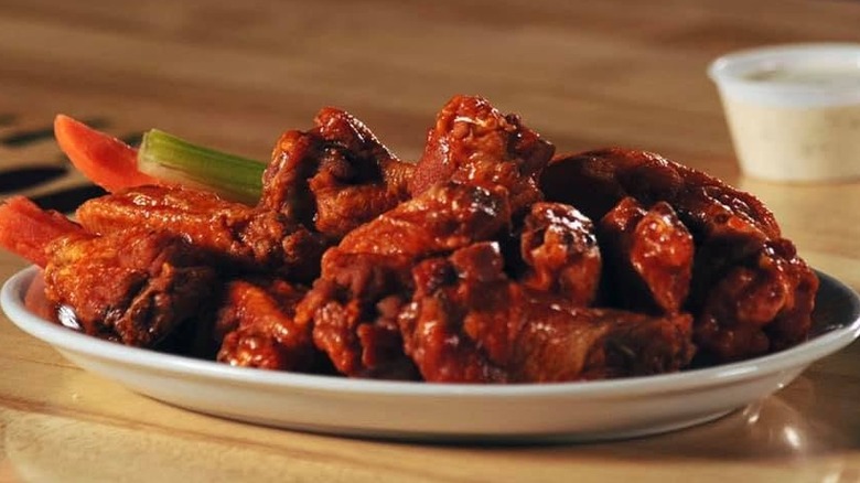 Pile of chicken wings next to pepper and celery slices with sauce in the background