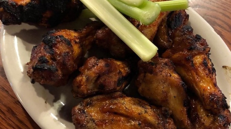 Pile of charred wings with celery sticks on a white plate