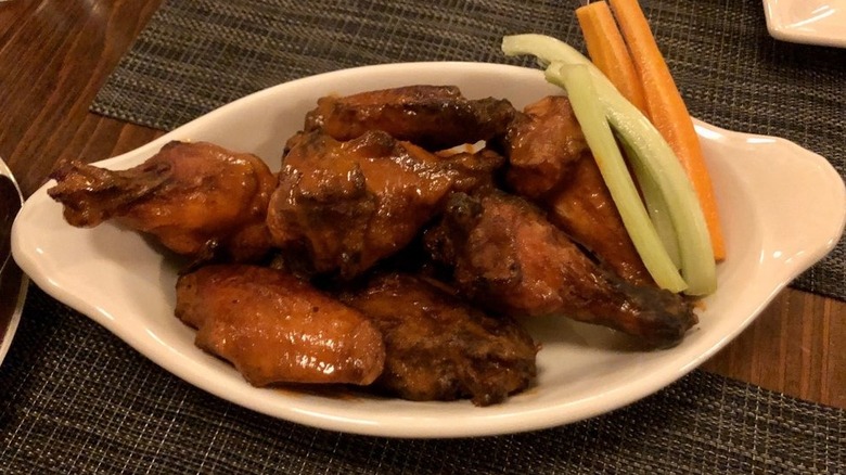 White bowl of saucy wings next to carrot and celery sticks