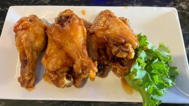 White plate with seasoned chicken wings next to a piece of lettuce