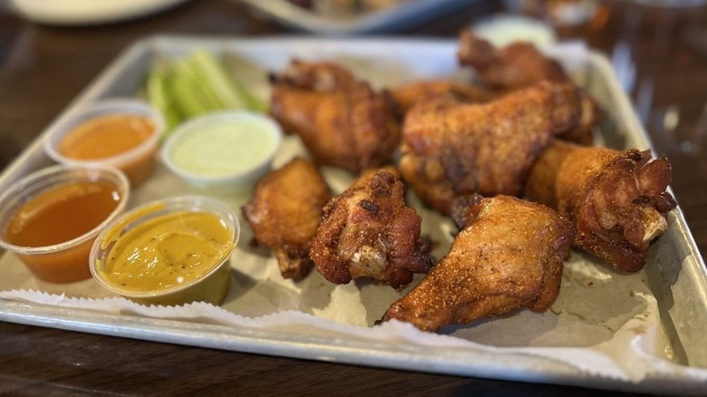 Tray of seasoned chicken wings with four sauces and celery sticks