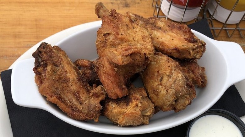 White bowl of fried chicken wings next to ketchup and ranch and mustard