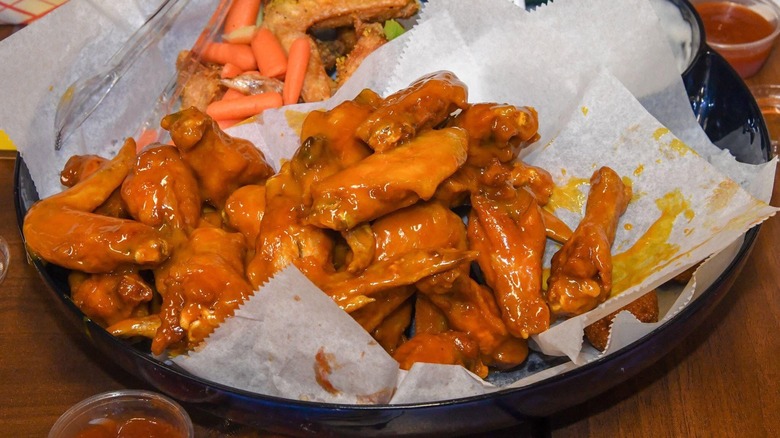 Bowl of saucy wings on top of sheet of parchment paper