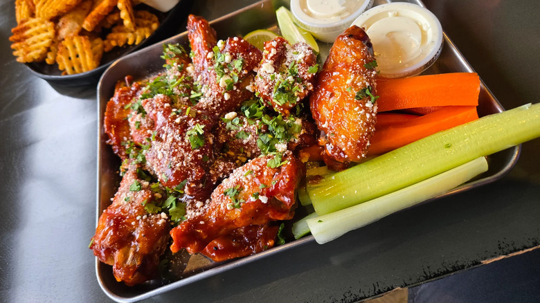 Tray of seasoned and saucy wings with ranch, carrots, celery, and fries