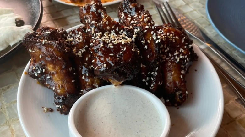 White plate with Korean chicken wings next to dipping sauce