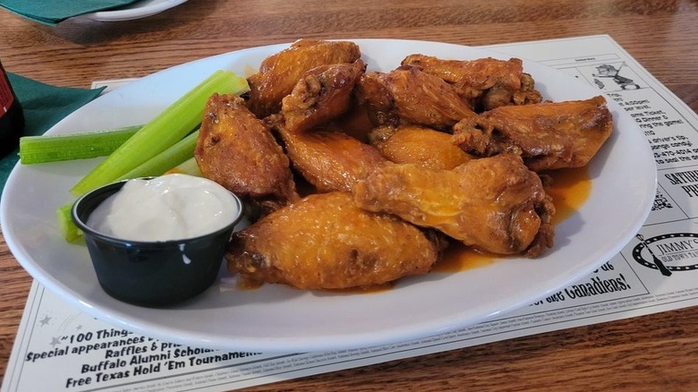 White plate of buffalo chicken wings next to celery sticks and blue cheese