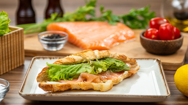 Croissant with smoked salmon and leafy greens on a plate in front of raw salmon on cutting board