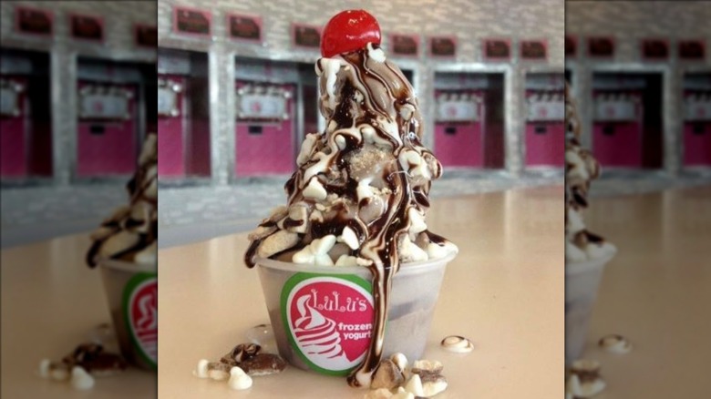 cup of lulus froyo with syrup dripping out of it and surrounded by chopped nuts