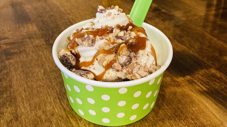 green and white polka dot cup of froyo with caramel syrup and cookie crumbles