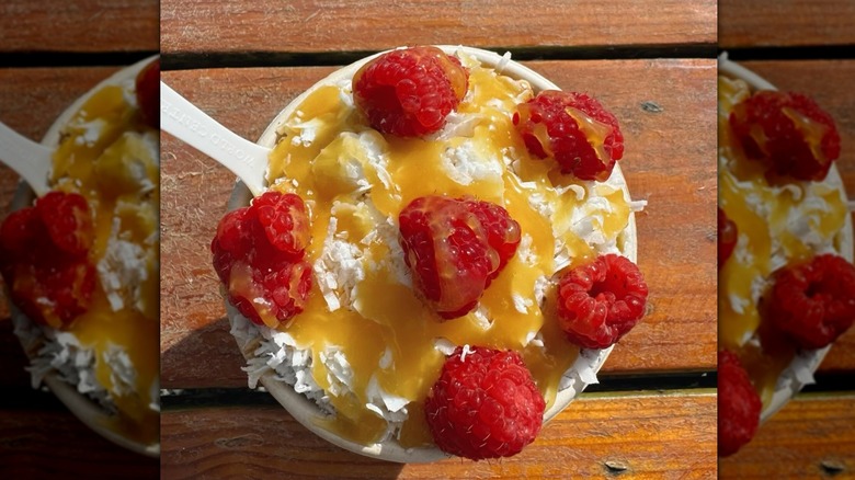 cup of froyo topped with coconut, raspberries, and pineapple syrup