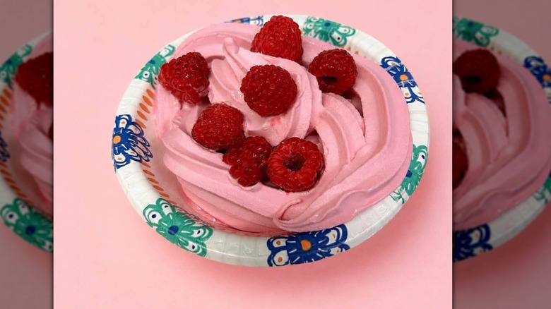 paper bowl full of pink froyo topped with raspberries against a pink background
