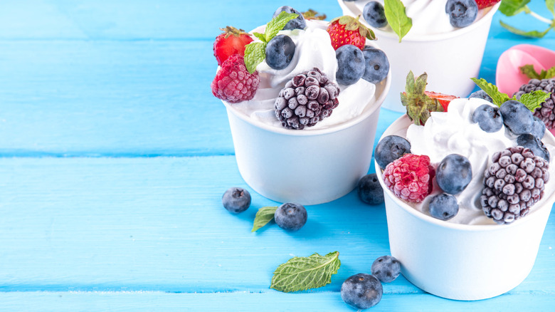 three paper cups of froyo topped with frozen fruit and mint leaves