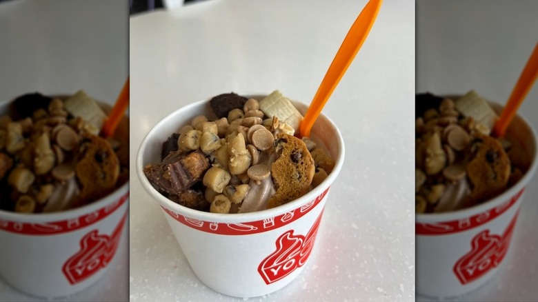 cup of froyo topped with banana slices, chocolate chip cookies, cookie dough, and peanut butter chips
