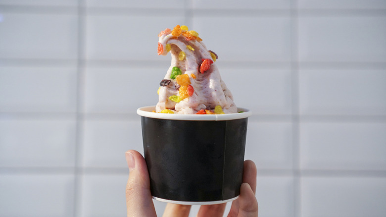 hand holding a black paper cup of pink froyo with cereal toppings