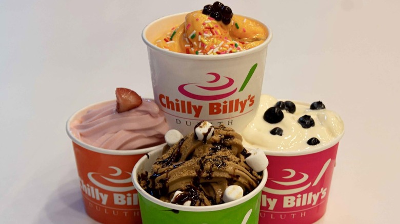 four cups of froyo with different flavors and toppings like marshmallows, boba, strawberries, and sprinkles