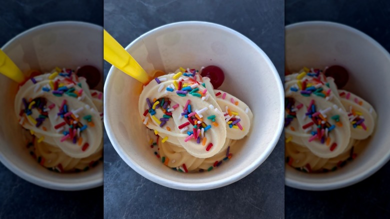 cup of white froyo with sprinkles, a cherry, and a yellow spoon