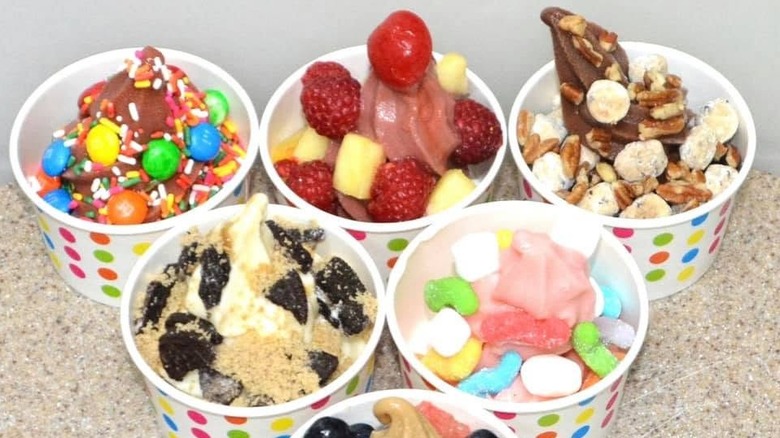 six polka dot cups of froyo with a variety of many different toppings