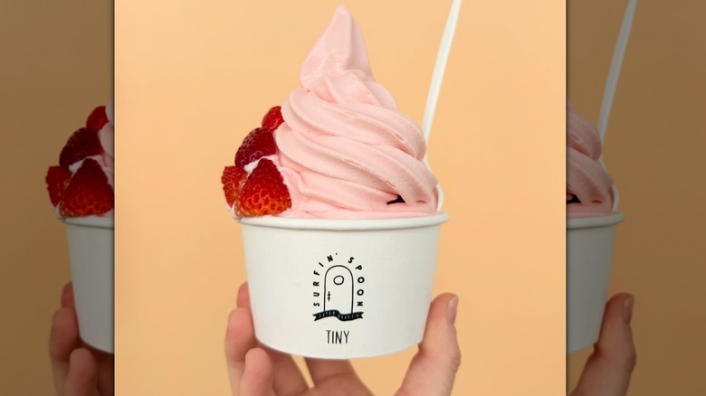 paper cup of strawberry swirl froyo with a white plastic spoon and chunks of fresh strawberries