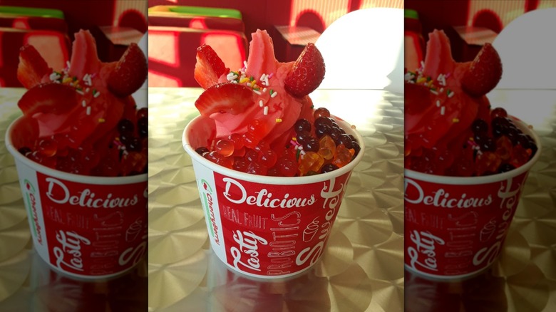 paper cup of red froyo with sprinkles, fresh strawberry chunks, boba, and gummy bears